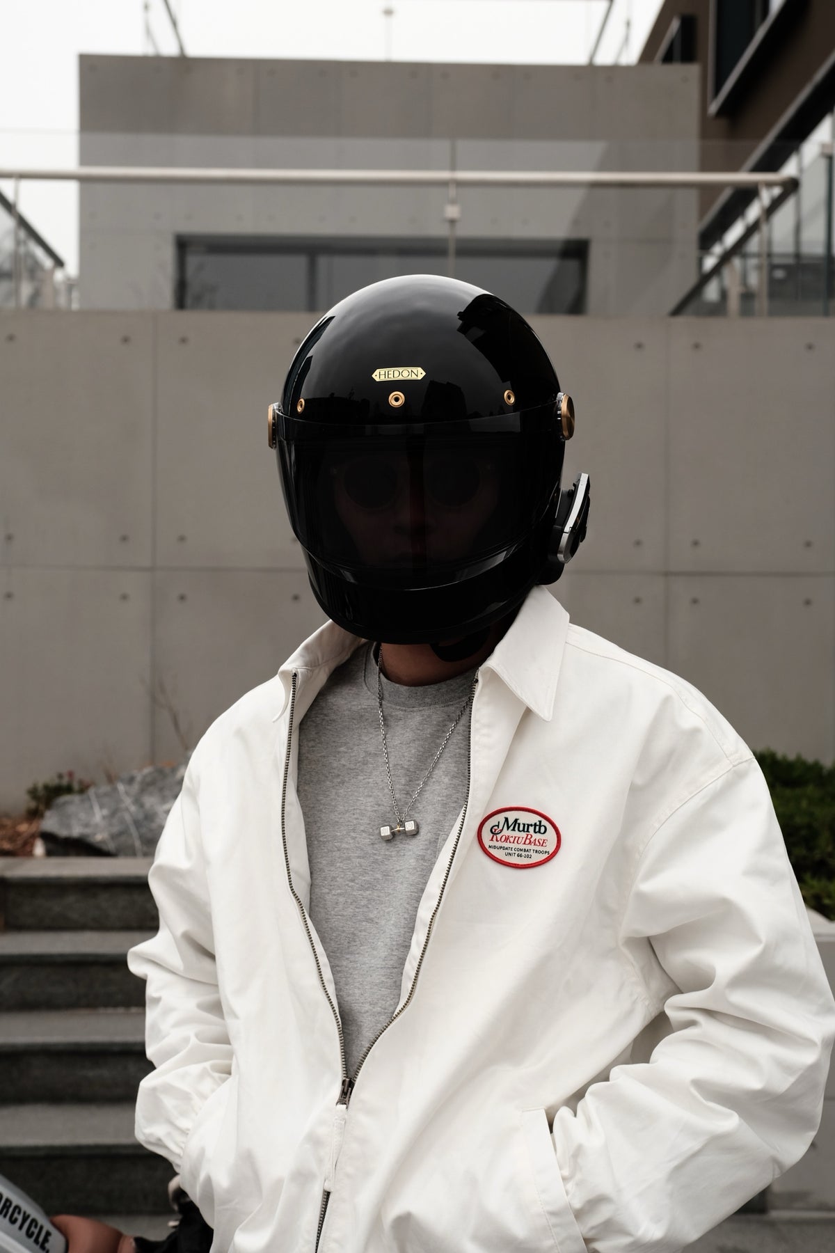 Person wearing a silver dumbbell pendant necklace with a black motorcycle helmet