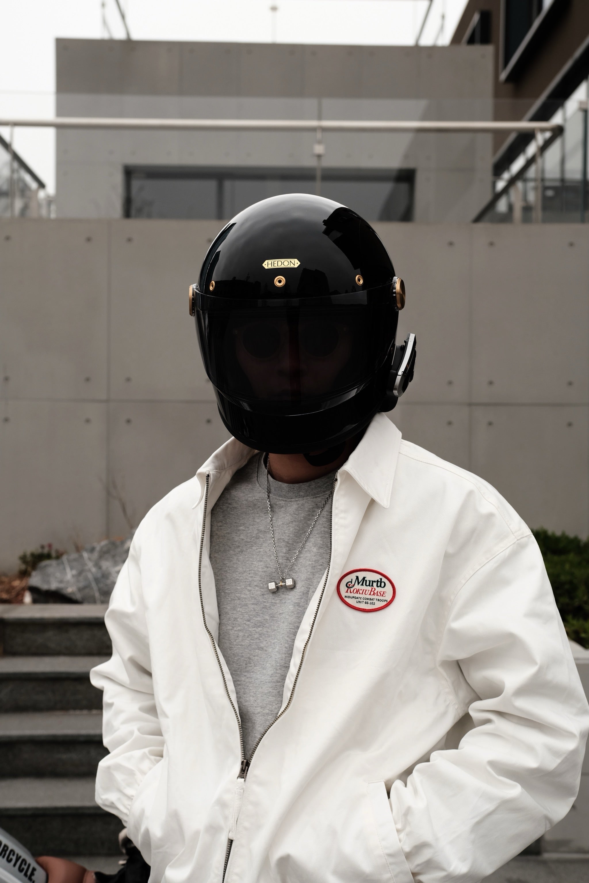 Person wearing a silver dumbbell pendant necklace with a black motorcycle helmet