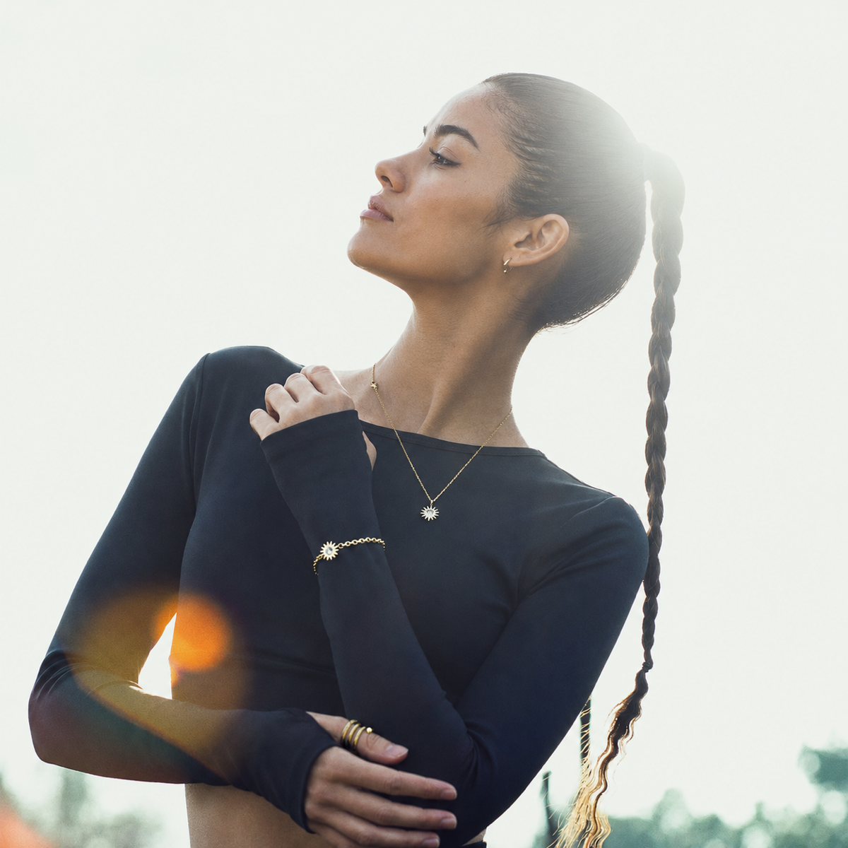 Latina model wearing gold Solstice Sun pendant necklace in backlight